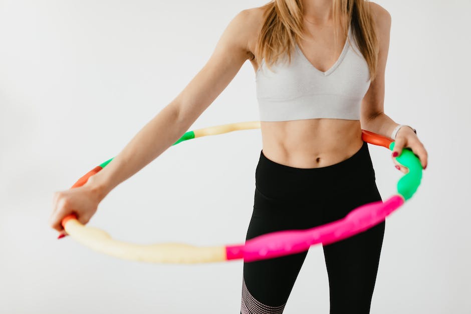 Crop faceless fit lady in black leggings and sports bra practicing fitness exercises with hula hoop against gray background