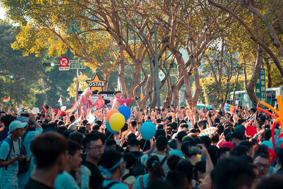 Crowd of unrecognizable Asian people standing on city street with colorful balloons and watching performance during festival on sunny day