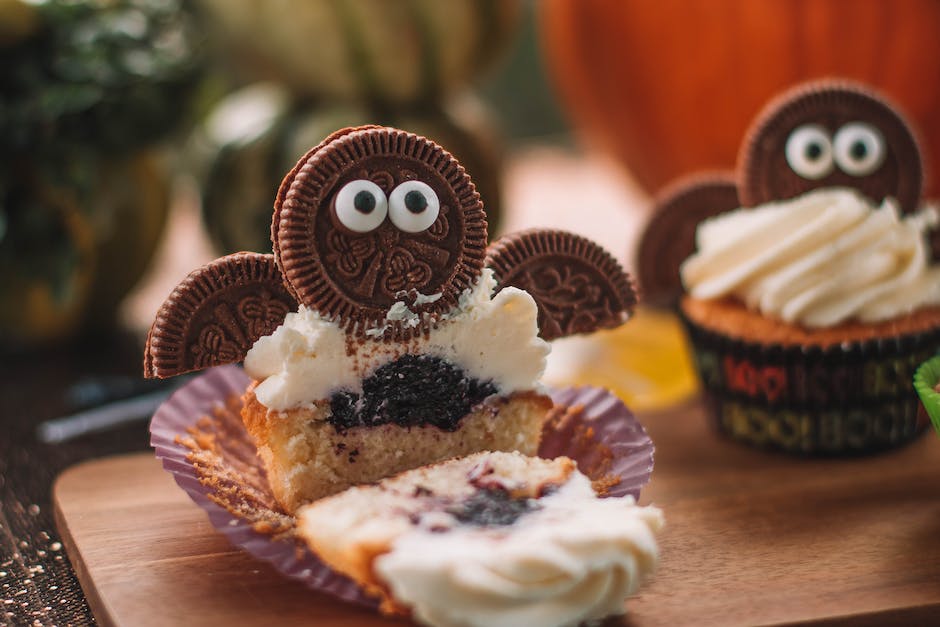 Tasty cut cupcake with sweet filling and frosting decorated with cookie placed on wooden cutting board in room on blurred background